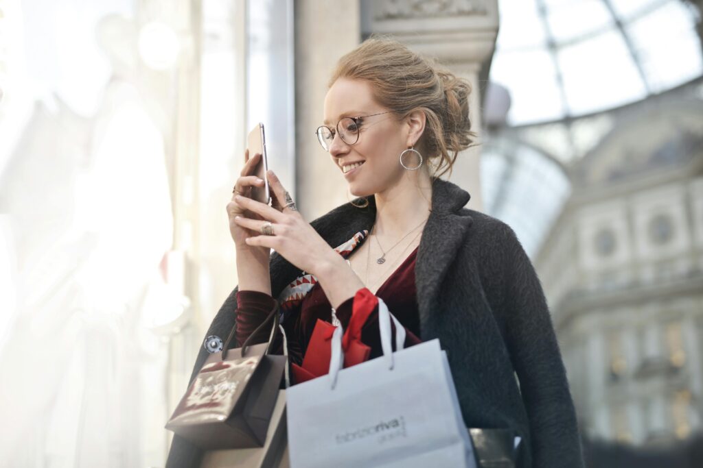 Stylish woman with shopping bags using smartphone in Milano, Italy. Perfect urban tech and fashion capture.